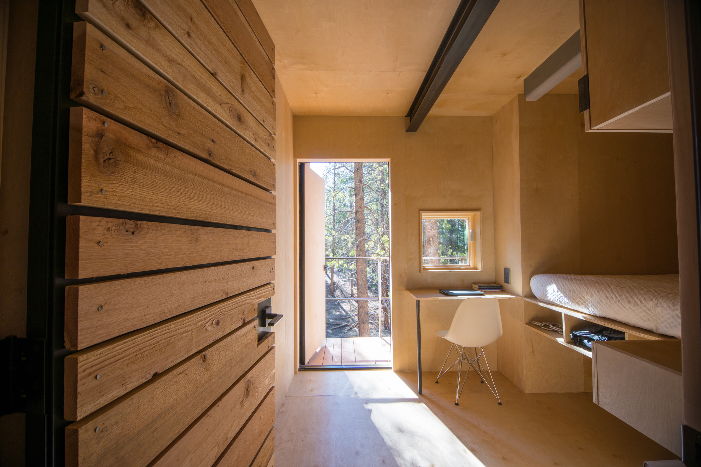 Mountain Modern Cabins — 200sf interior showing integrated desk, elevated sleeping platform with storage below, window to pine forest