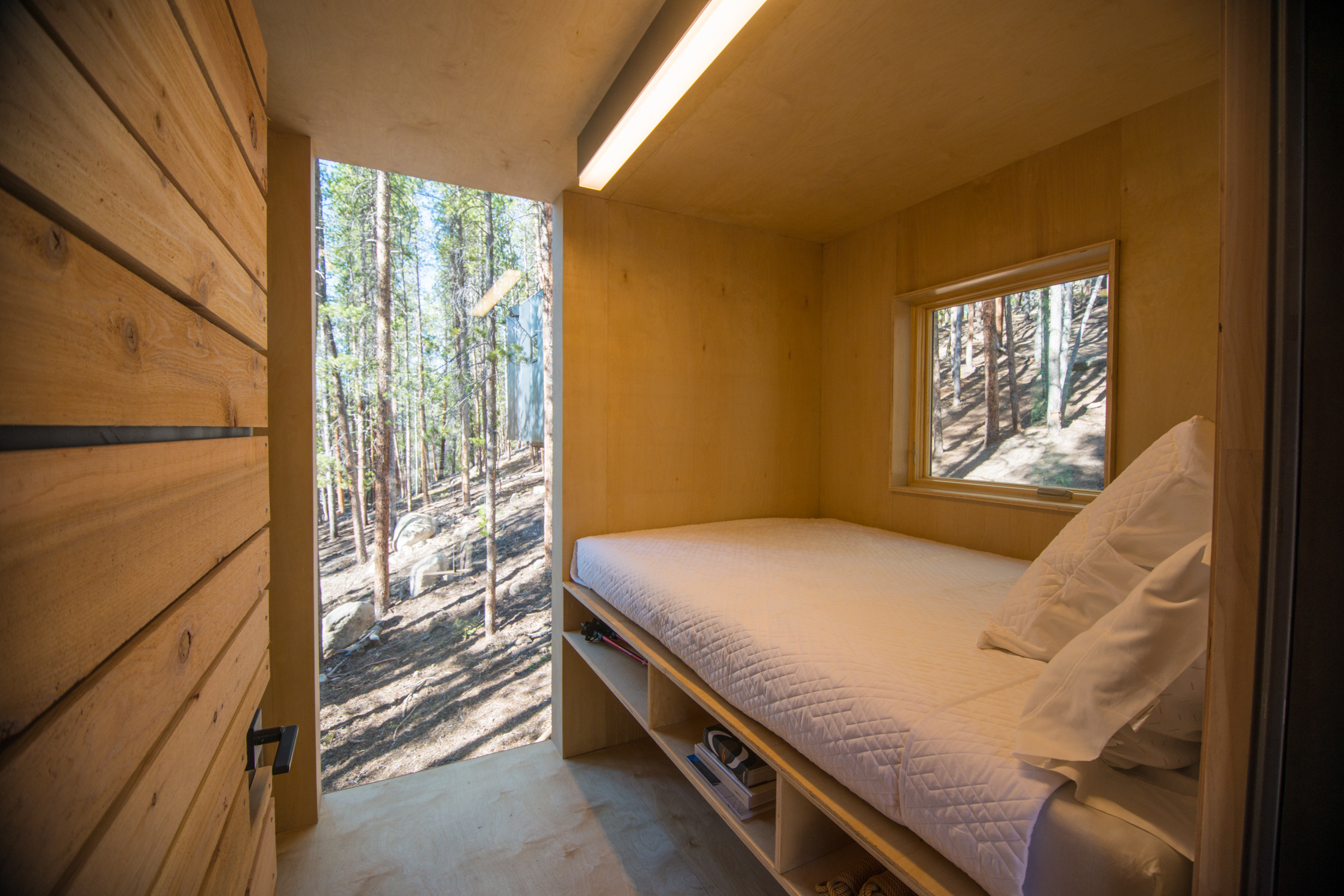 Mountain Modern Cabins — interior storage wall open showing integrated shelving, desk workspace, climbing helmet, hot rolled steel backing panel