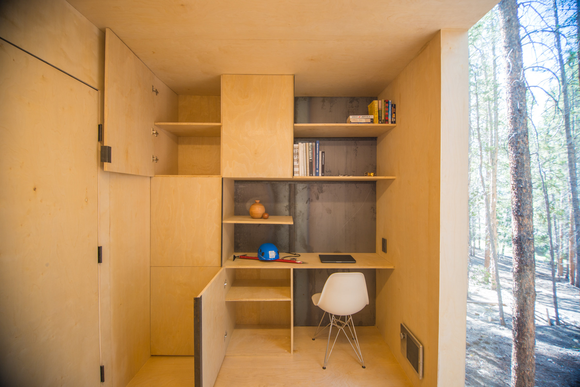 Mountain Modern Cabins — bed alcove with exposed steel moment frame beam, open porch door to cedar deck and pine forest beyond